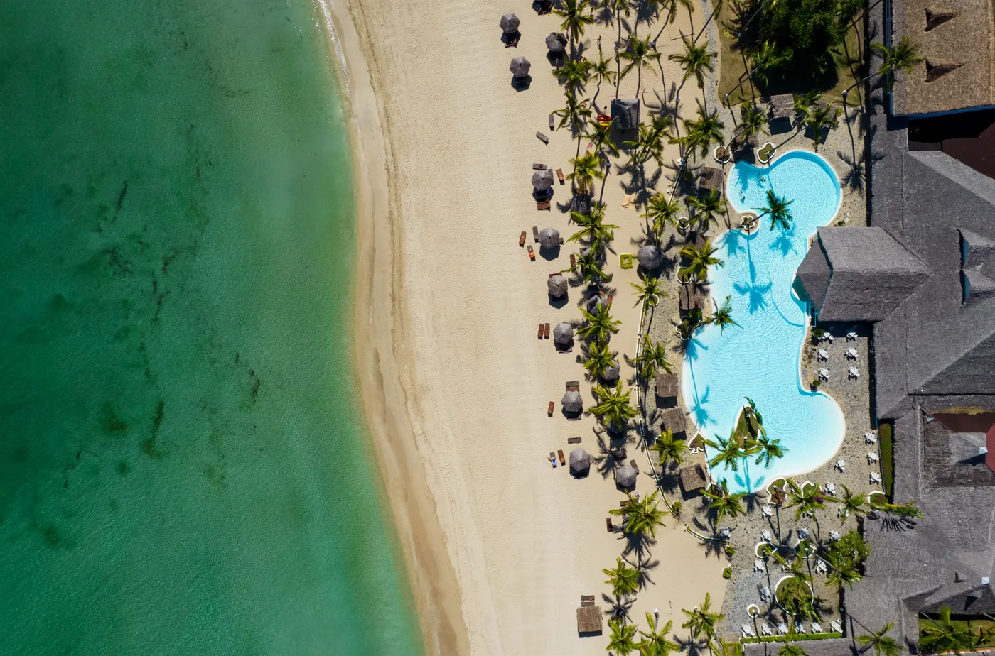 Il mare, la spiaggia e una piscina fra le palme, visti dall’alto